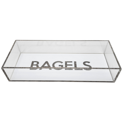 The Eye Candy Bagel Tray is a rectangular, clear silver marble acrylic box with "BAGELS" in bold capitals on the inside bottom. Food safe and lidless, it offers a modern touch for serving bagels.