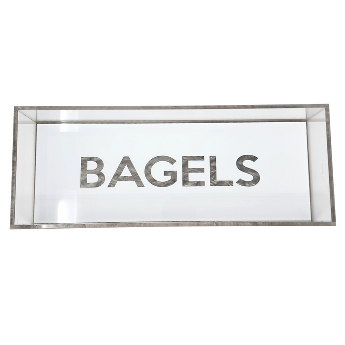 The Eye Candy Bagel Tray is a rectangular glass display case with "BAGELS" in bold letters on the front, a food-safe acrylic tray for bagels, and stylish silver marble acrylic accents.