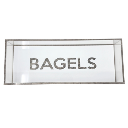 The Eye Candy Bagel Tray is a rectangular glass display case with "BAGELS" in bold letters on the front, a food-safe acrylic tray for bagels, and stylish silver marble acrylic accents.