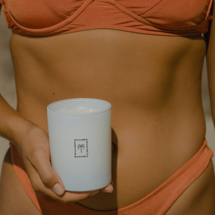 Person wearing an orange bikini holding a white candle with text on it.