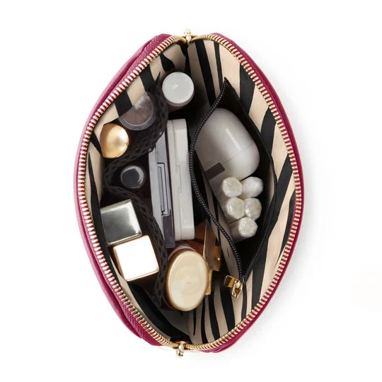 Wine/Zebra, An open makeup bag with a deep burgundy exterior, gold zipper, and a beige-and-black zebra-print interior, shown filled with cosmetics on a white background.