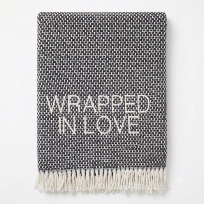 A Soft Idea’s Wrapped in Love Throw is a folded dark gray woven blanket with white fringed edges. Super soft, machine washable, and “WRAPPED IN LOVE” stitched in white—perfect for gifting.